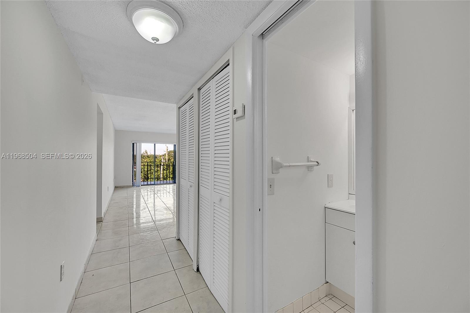 A hallway with white tile floors leads to a room with a balcony view — 650 NE 149th St # 406A, Miami FL 33161, MIAMI, FL