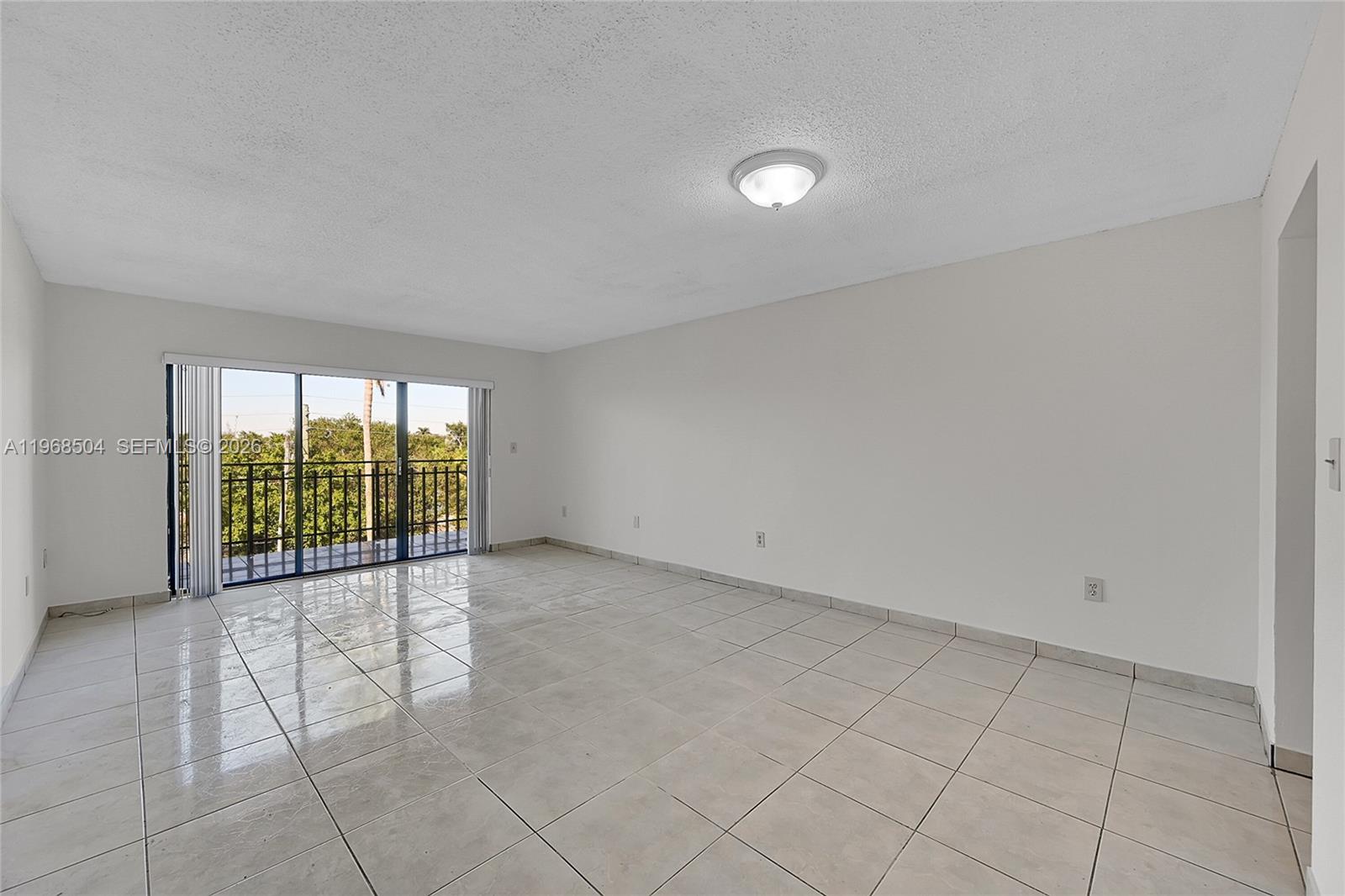 An empty room features white walls, light-colored tile flooring, a ceiling light, and a sliding glass door — 650 NE 149th St # 406A, Miami FL 33161, MIAMI, FL