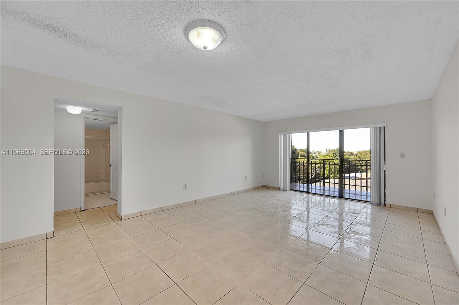 An empty room with beige tile flooring, a ceiling light, and a sliding glass door — 650 NE 149th St # 406A, Miami FL 33161, MIAMI, FL