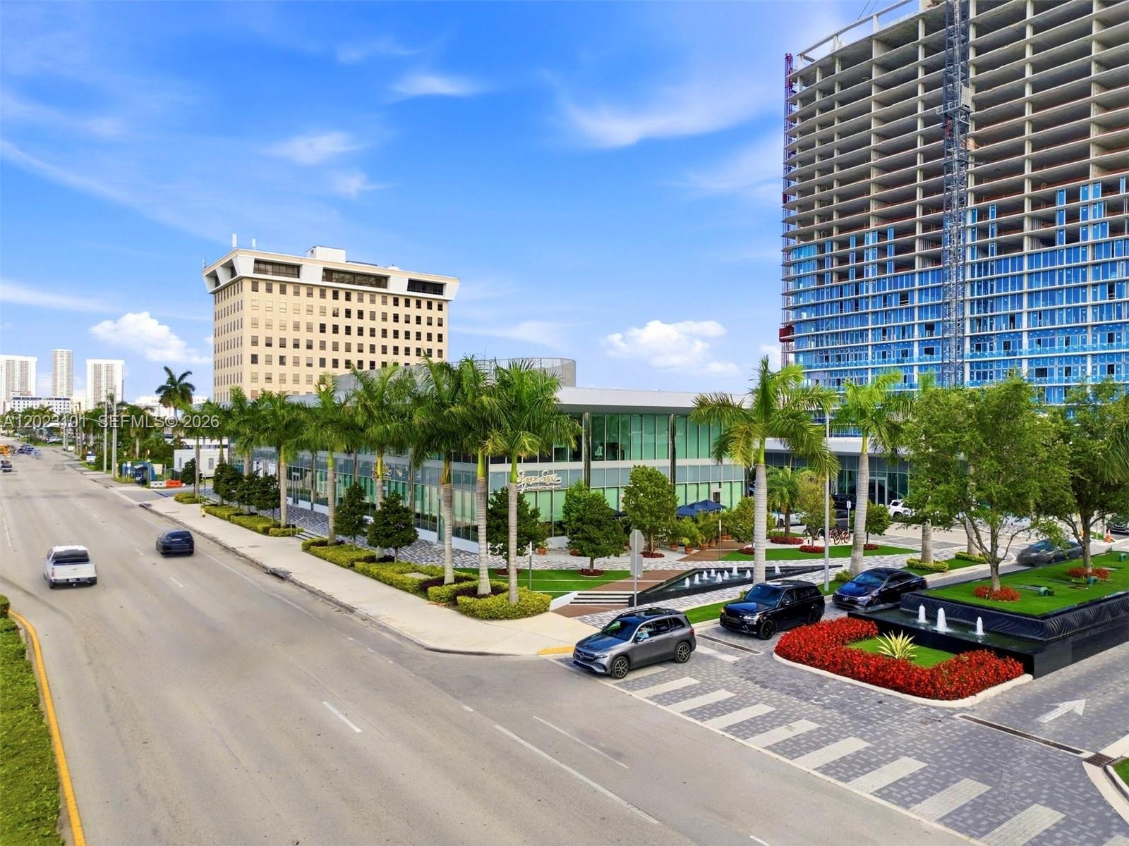 An aerial view shows a modern glass building with palm trees, fountains, and surrounding streets — 1006 E Hallandale Beach Blvd # 103, Hallandale Beach FL 33009, HALLANDALE BEACH, FL