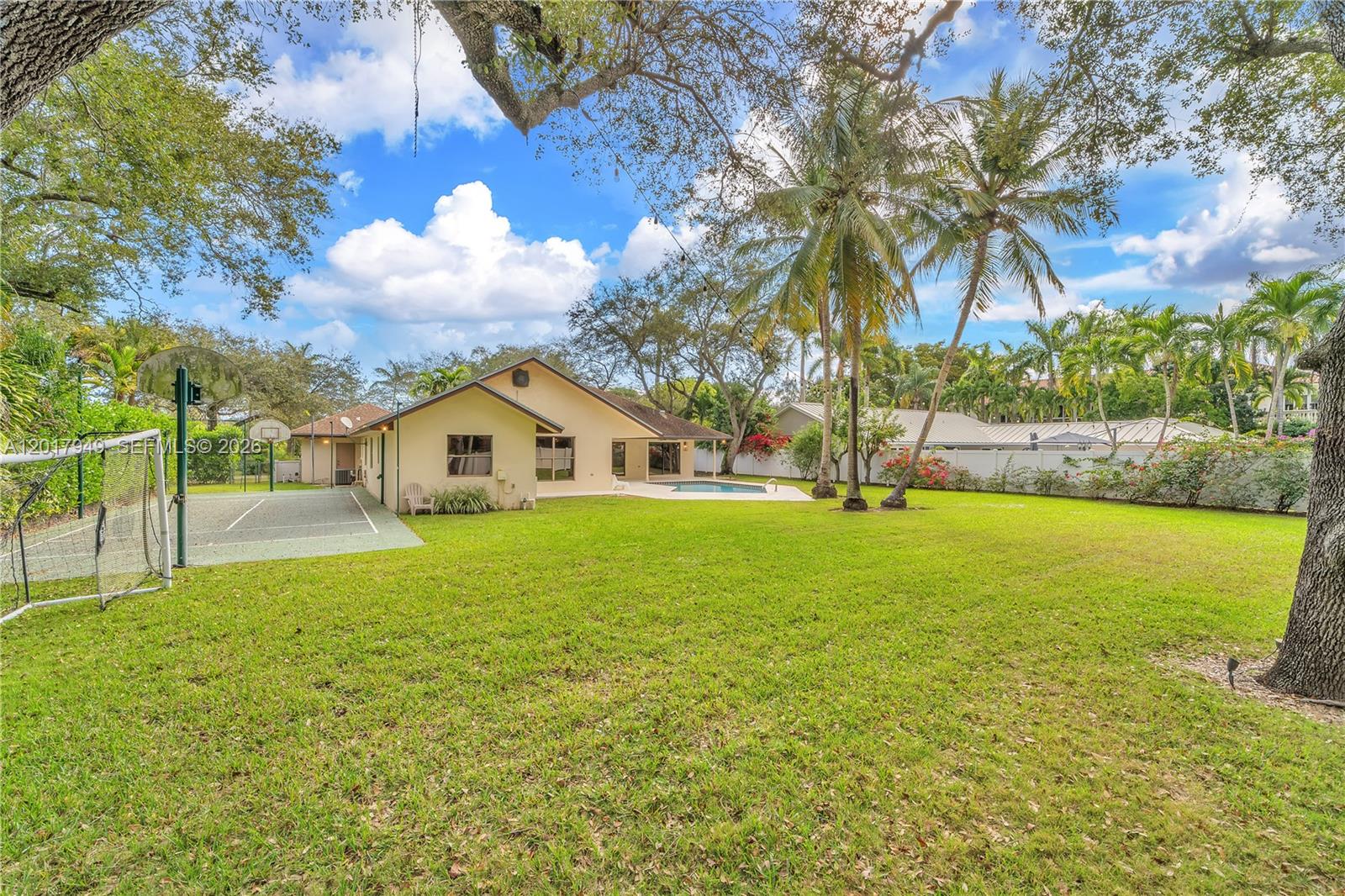 A backyard features a swimming pool, a tennis court, and palm trees behind a house — 10330 SW 58th Ct, Pinecrest FL 33156, PINECREST, FL