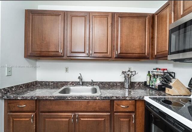 A kitchen features dark wood cabinets, a stainless steel sink, and a dark laminate countertop — 185 Normandy # D, Delray Beach FL 33484, DELRAY BEACH, FL