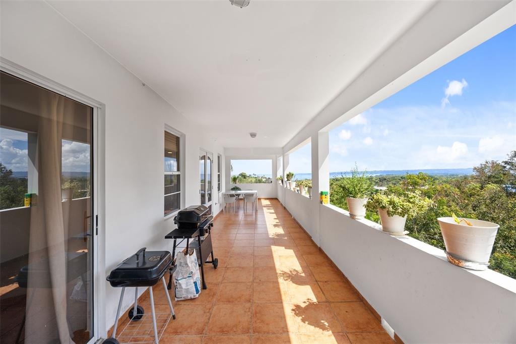 A long, tiled balcony features two charcoal grills and potted plants overlooking a scenic landscape — 3rd Floor PUNTA LIBERTAD CONDOMINIO UNIT 3, RINCON, PR