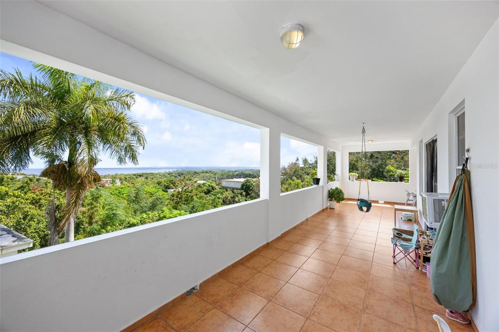 A long, tiled balcony features white walls, a hanging swing, and panoramic ocean views — 3rd Floor PUNTA LIBERTAD CONDOMINIO UNIT 3, RINCON, PR