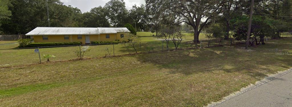 A yellow single-story house with a metal roof sits behind a chain-link fence — 817 SW 143RD STREET, NEWBERRY, FL