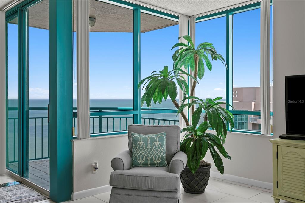 A gray armchair and a potted plant sit in a sunroom with floor-to-ceiling windows — 1540 GULF BOULEVARD UNIT 2107, CLEARWATER BEACH, FL