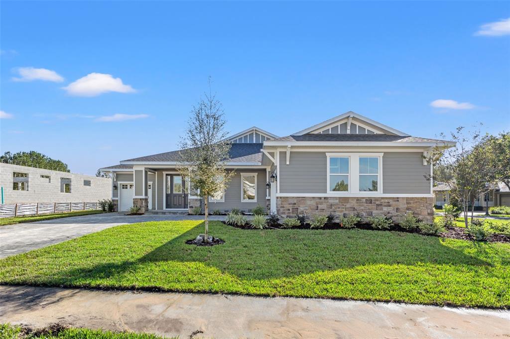 A single-story house with gray siding, stone accents, and a front lawn under a blue sky — 19486 SHELTERED HILL DRIVE, BROOKSVILLE, FL
