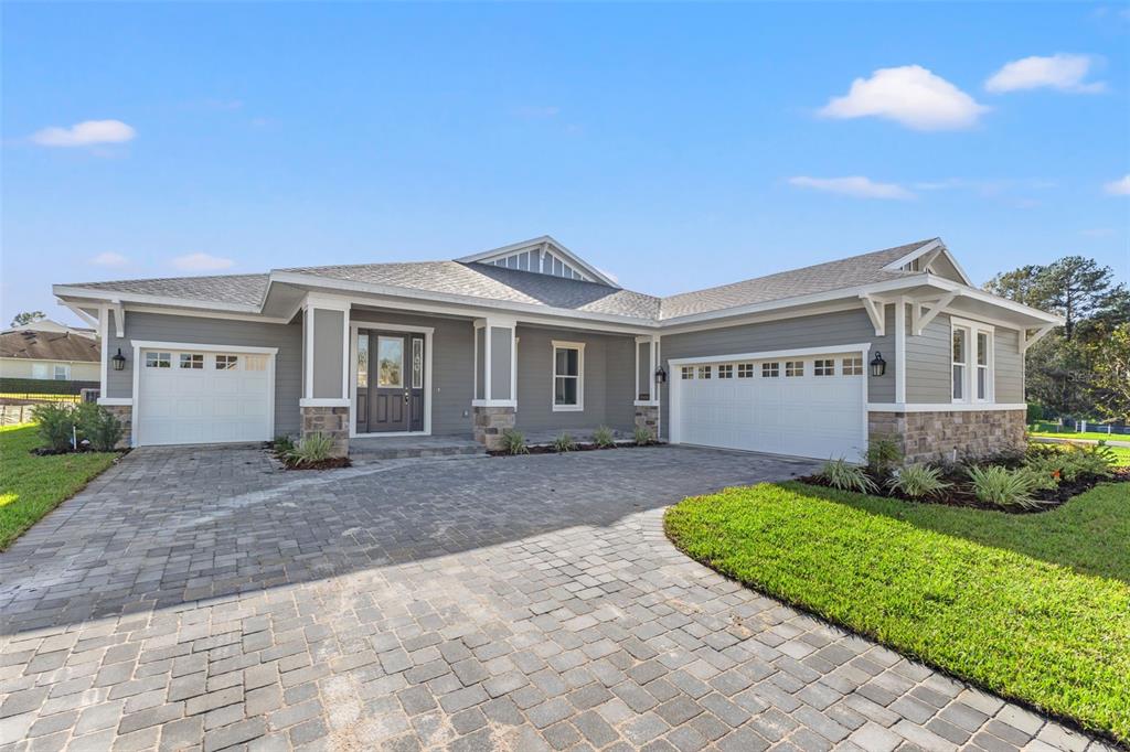 A gray single-story house with a stone-accented facade, white trim, and a paved driveway — 19486 SHELTERED HILL DRIVE, BROOKSVILLE, FL