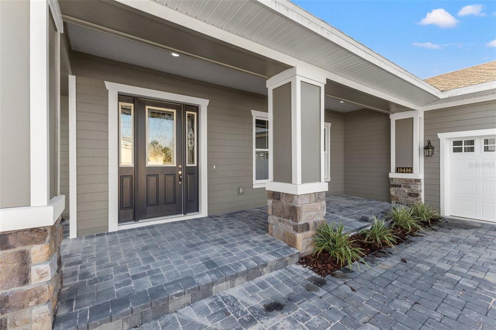 A front porch with stone-based columns, gray siding, and a dark door with glass panels — 19486 SHELTERED HILL DRIVE, BROOKSVILLE, FL