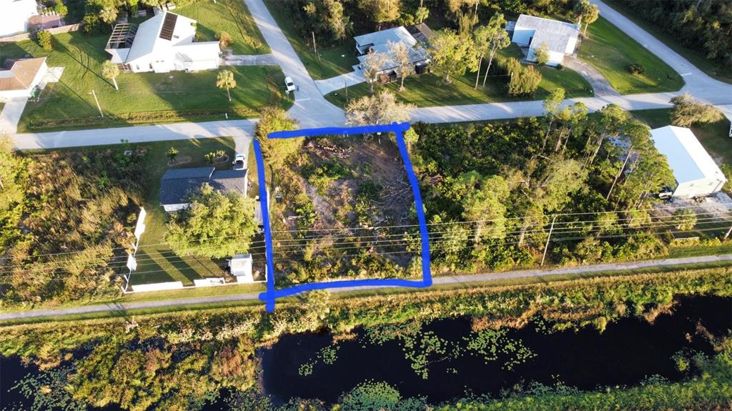 An aerial view shows a vacant, partially cleared residential lot outlined in blue near a canal — 3419 SWANEE ROAD, PORT CHARLOTTE, FL