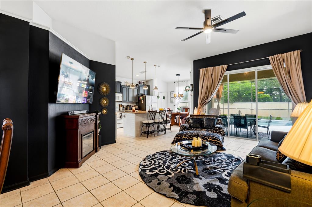 An open-concept living room and kitchen featuring dark accent walls, tile flooring, and a fireplace — 8066 KING PALM CIRCLE, KISSIMMEE, FL
