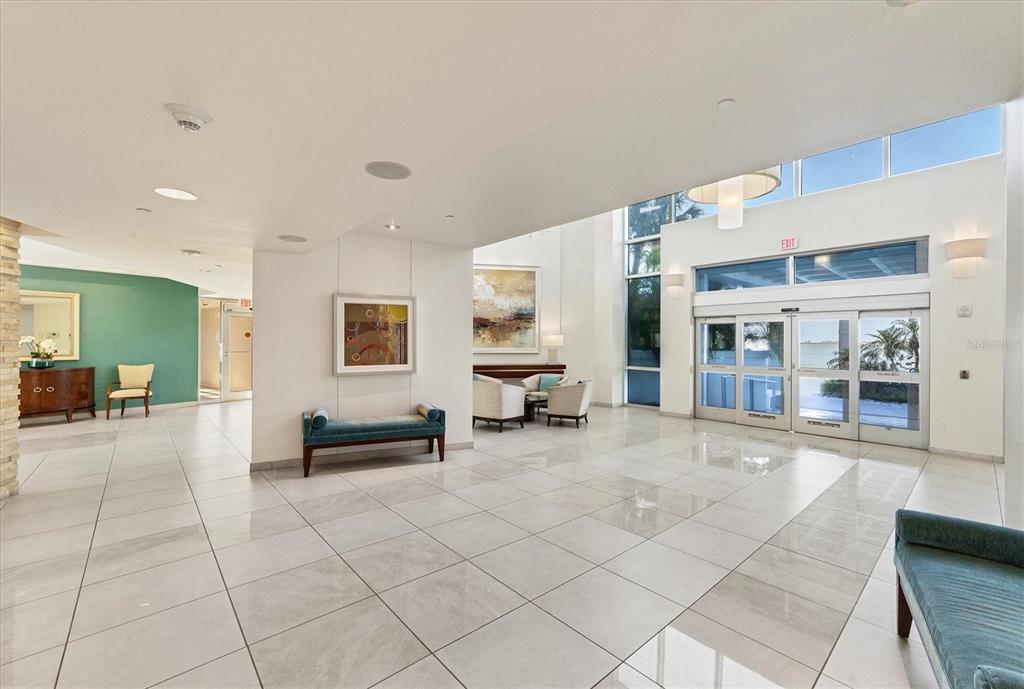 A bright, modern lobby features white tiled floors, high ceilings, and glass sliding entrance doors — 988 BLVD OF THE ARTS UNIT 1816, SARASOTA, FL