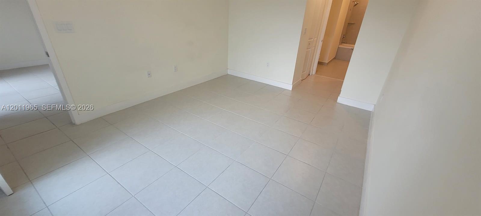 An empty room with light-colored tile flooring and white walls leads to a bathroom — 8001 NW 41st St # 405, Doral FL 33166, DORAL, FL