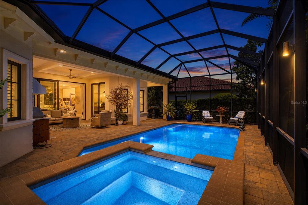 A screened-in patio features a swimming pool, a raised spa, and outdoor seating at dusk — 7952 MATERA COURT, LAKEWOOD RANCH, FL