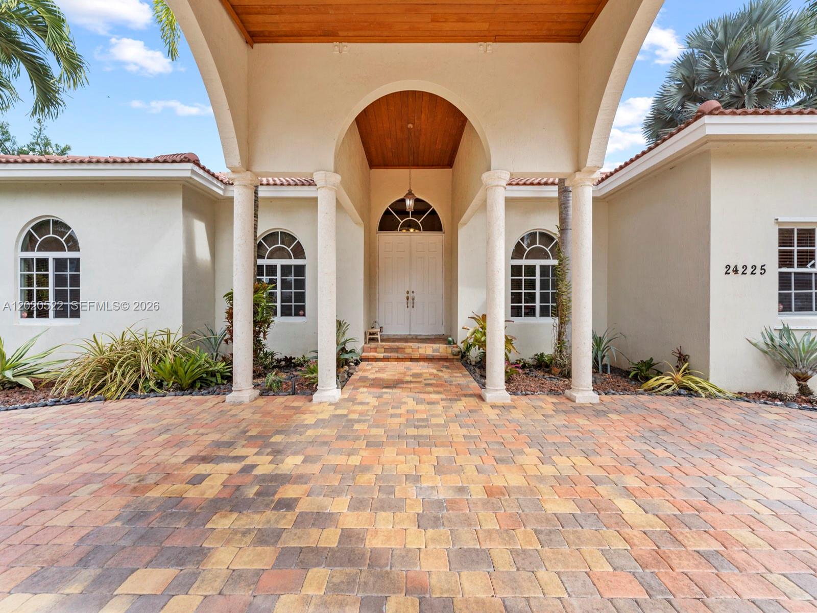 The exterior of a house features a paved driveway leading to a covered arched entryway — 24225 SW 198th Ave, Homestead FL 33031, HOMESTEAD, FL