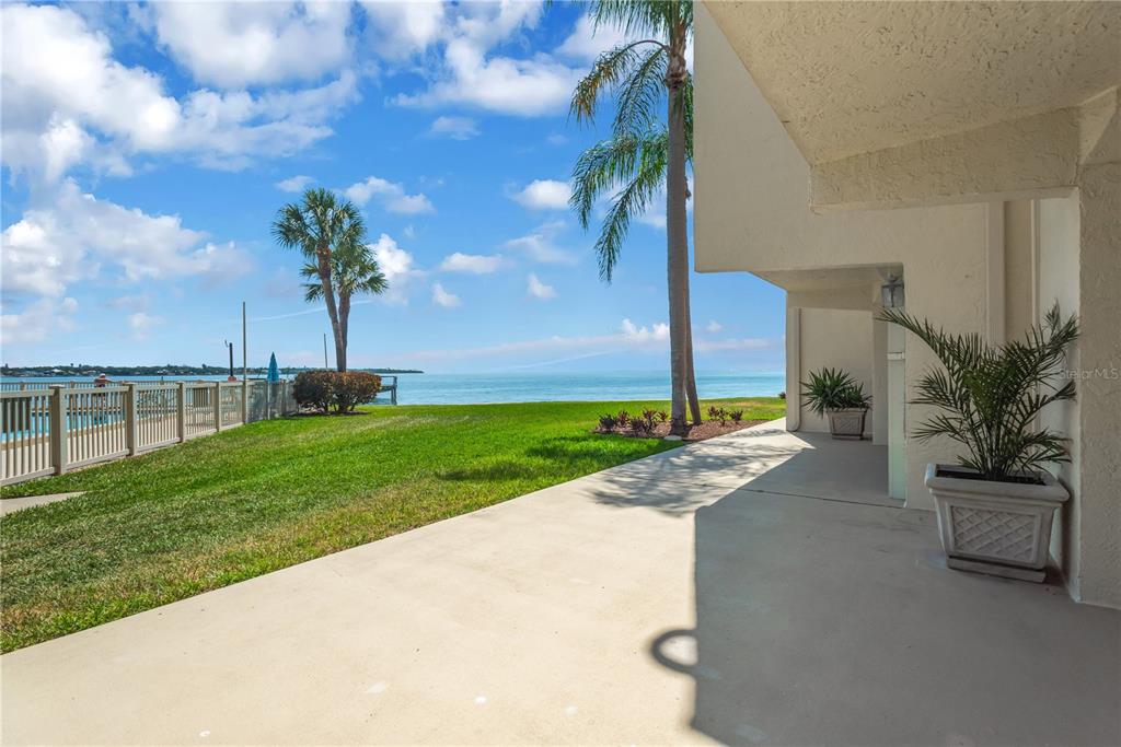 A concrete patio overlooks a grassy lawn, palm trees, and a calm body of water — 7520 SUNSHINE SKYWAY LANE S UNIT P5, ST PETERSBURG, FL