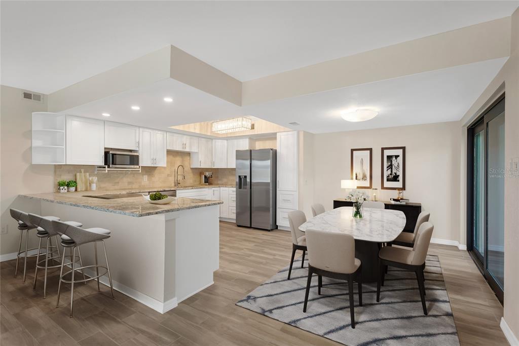 A kitchen with white cabinets and granite countertops opens to a dining area with seating — 7520 SUNSHINE SKYWAY LANE S UNIT P5, ST PETERSBURG, FL