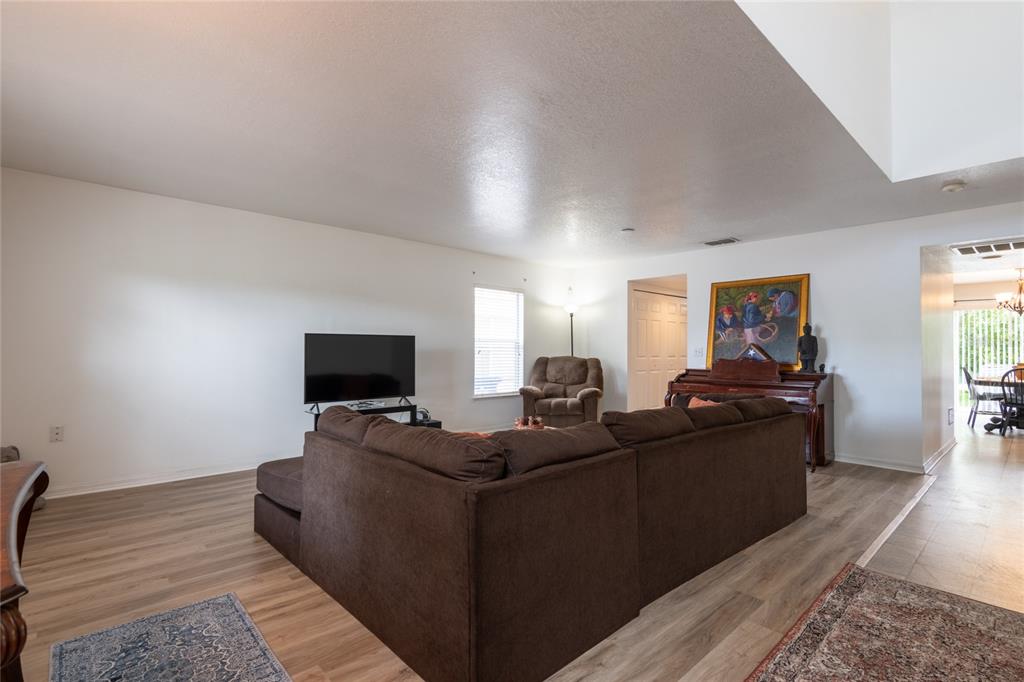 A living room features a brown sectional sofa, a television, and wood-look flooring — 3142 BELLERICAY LANE, LAND O LAKES, FL