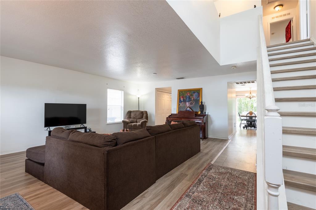 A living room with a brown sectional sofa, wood-look flooring, and a staircase — 3142 BELLERICAY LANE, LAND O LAKES, FL