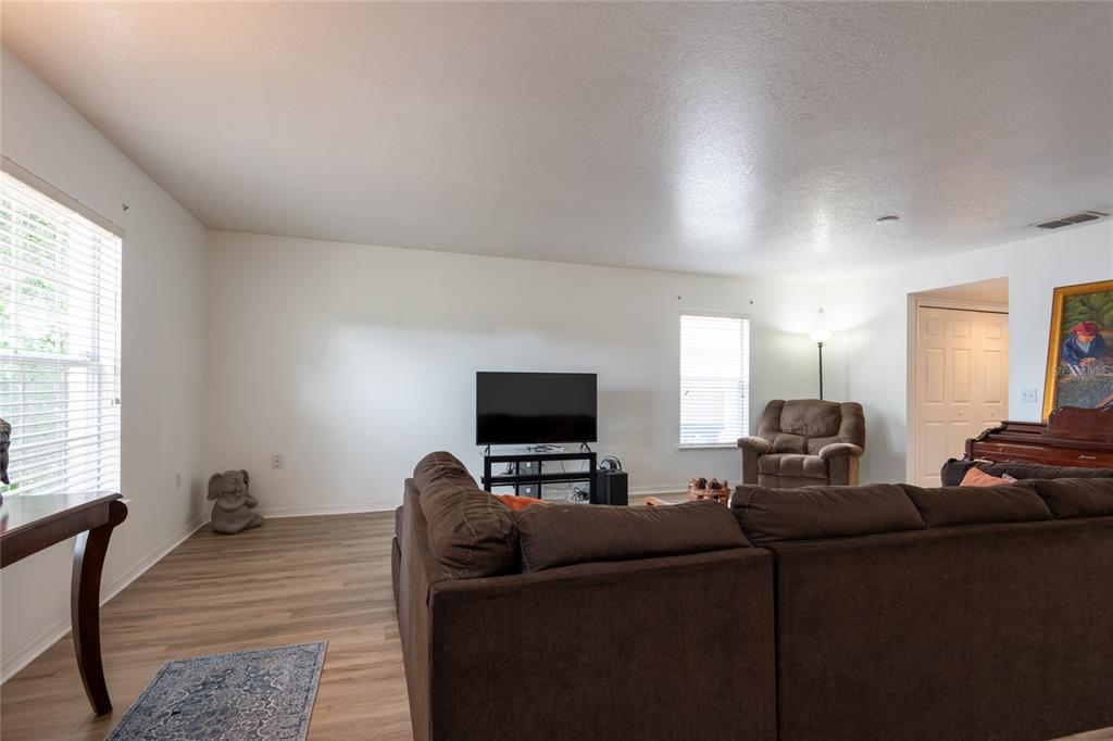 A living room features a brown sectional sofa, a television on a stand, and wood-look flooring — 3142 BELLERICAY LANE, LAND O LAKES, FL
