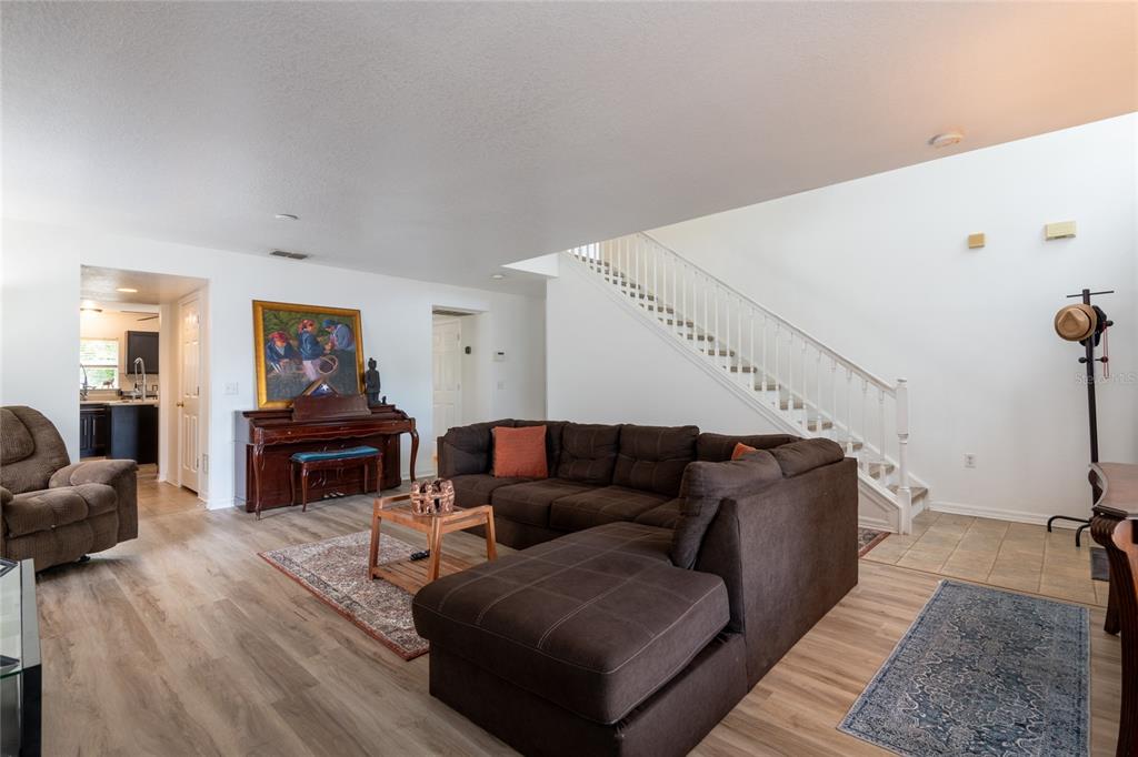 A living room features a brown sectional sofa, a piano, and a staircase — 3142 BELLERICAY LANE, LAND O LAKES, FL