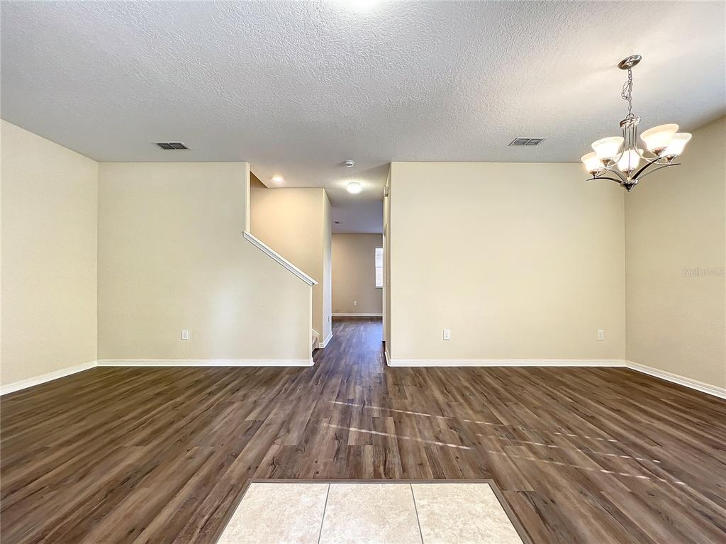 An empty room with wood-look flooring, beige walls, a chandelier, and a staircase — 14903 DRIFTWATER DRIVE, WINTER GARDEN, FL