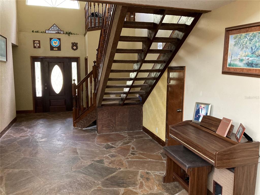 An entryway features a stone floor, a wooden staircase, and a piano near the front door — 2436 CR 416N, LAKE PANASOFFKEE, FL