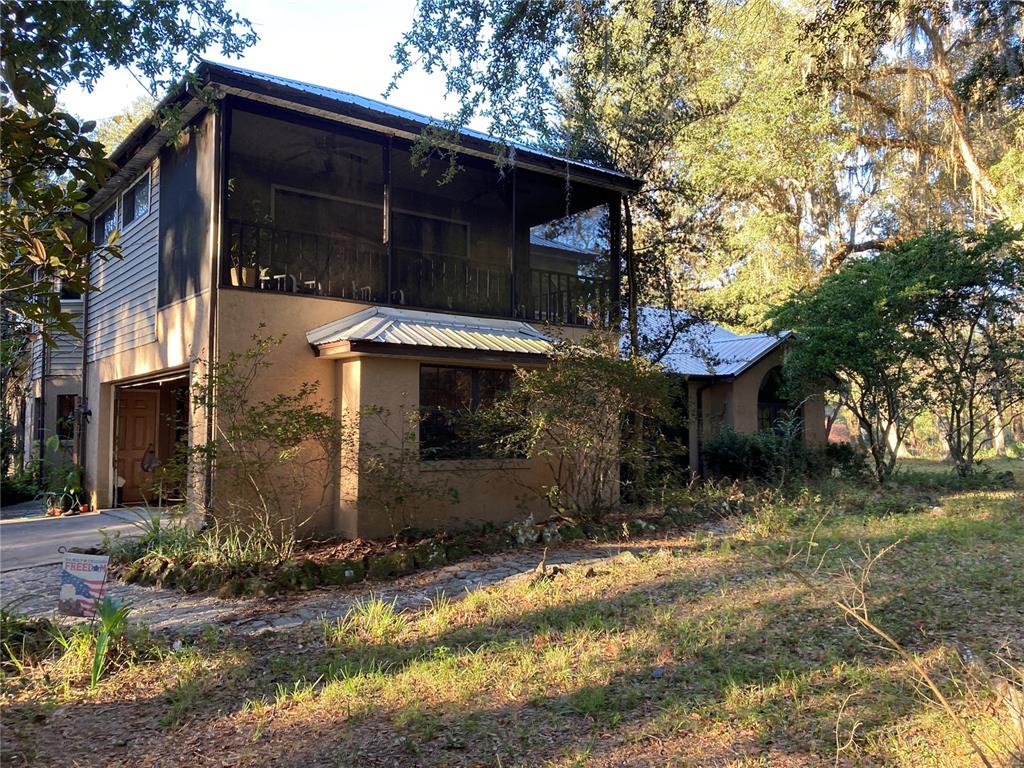 A two-story house with a screened-in upper balcony, tan stucco walls, and a metal roof — 2436 CR 416N, LAKE PANASOFFKEE, FL