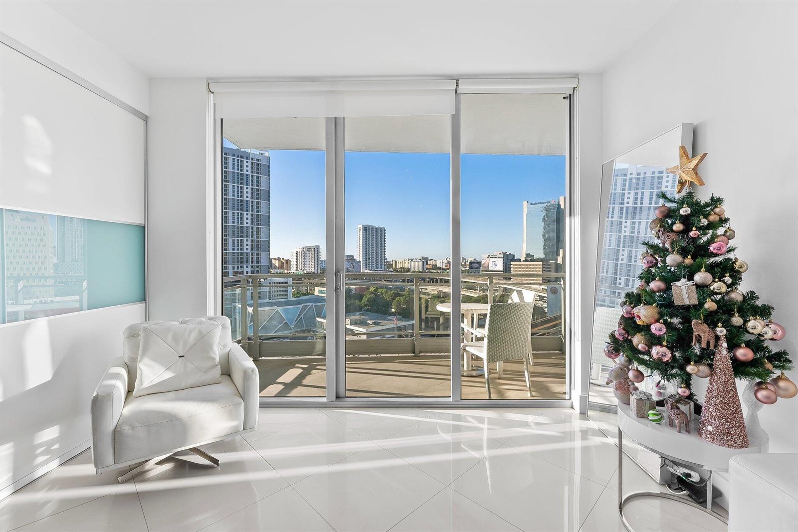A bright room with white tile floors, a white armchair, and a balcony overlooking city buildings — 90 SW 3rd Street # 1410, Miami FL 33130, MIAMI, FL