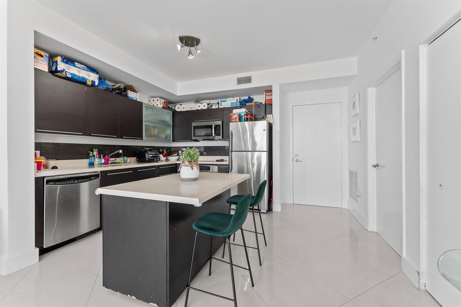 A modern kitchen features dark cabinetry, stainless steel appliances, a central island, and white tile flooring — 90 SW 3rd Street # 1410, Miami FL 33130, MIAMI, FL
