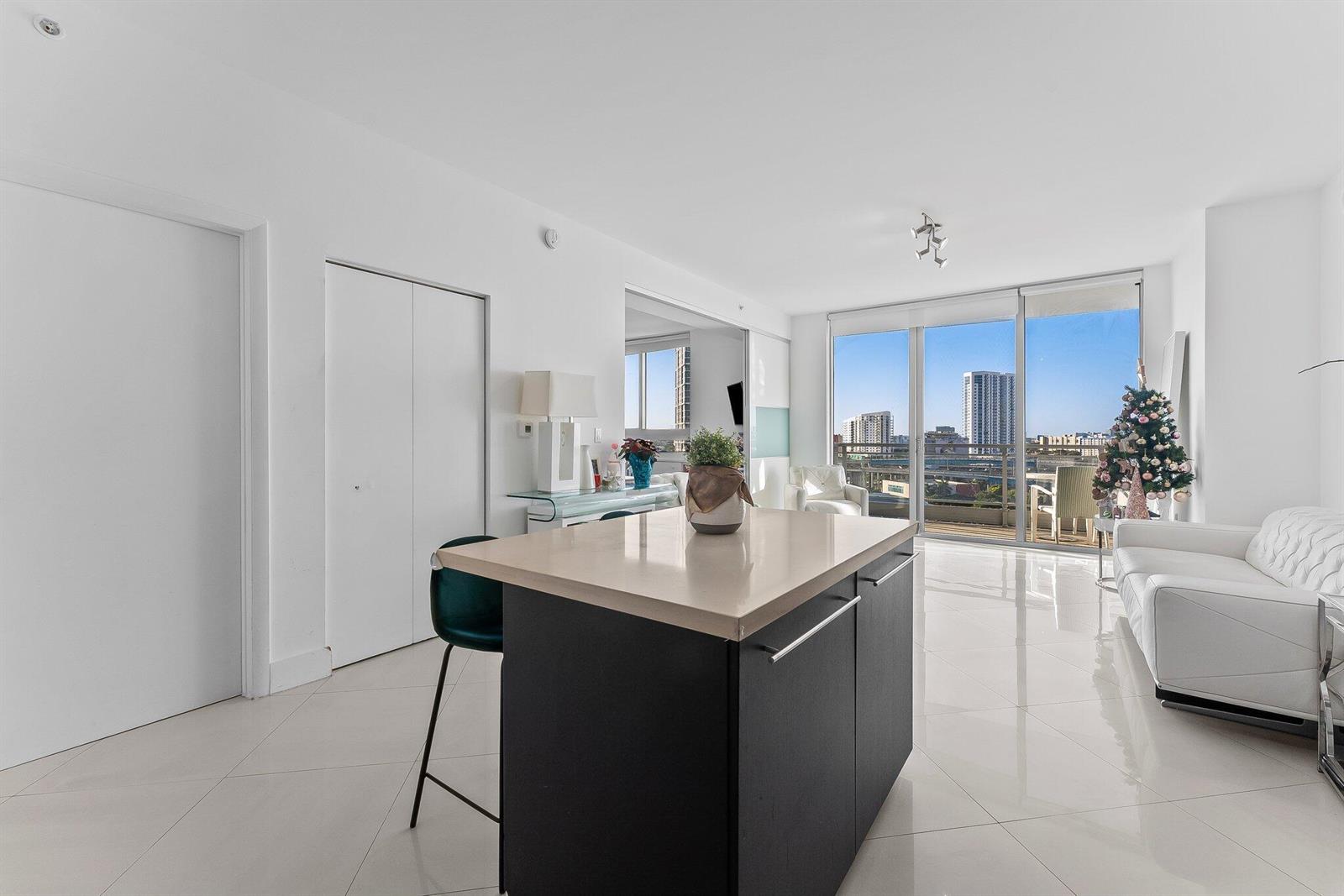 A modern apartment living area features a kitchen island, white tile floors, and balcony views — 90 SW 3rd Street # 1410, Miami FL 33130, MIAMI, FL
