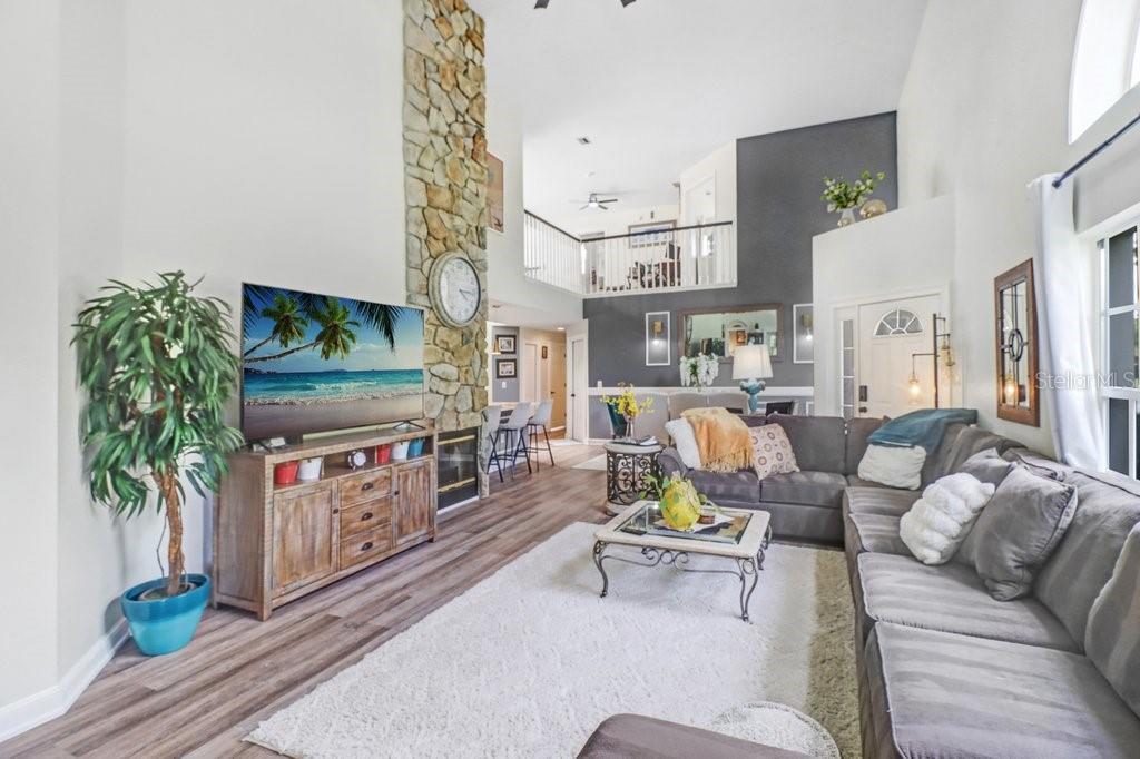 A living room features a stone fireplace, wood-look flooring, and a lofted second-floor balcony — 6049 GENTLE BEN CIRCLE, WESLEY CHAPEL, FL