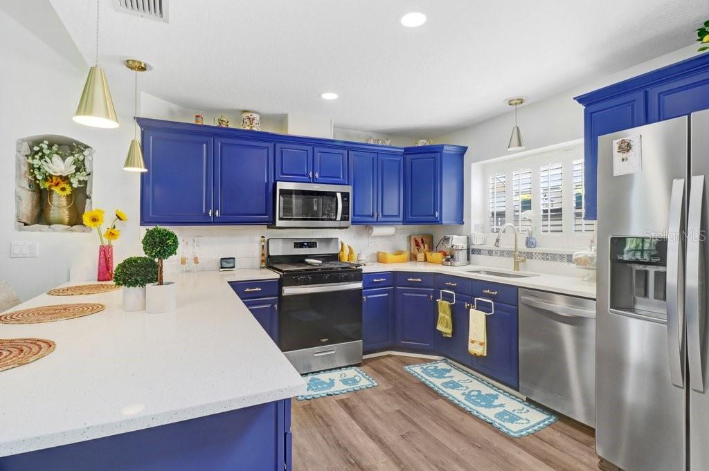 A kitchen features blue cabinets, white countertops, stainless steel appliances, and wood-look flooring — 6049 GENTLE BEN CIRCLE, WESLEY CHAPEL, FL
