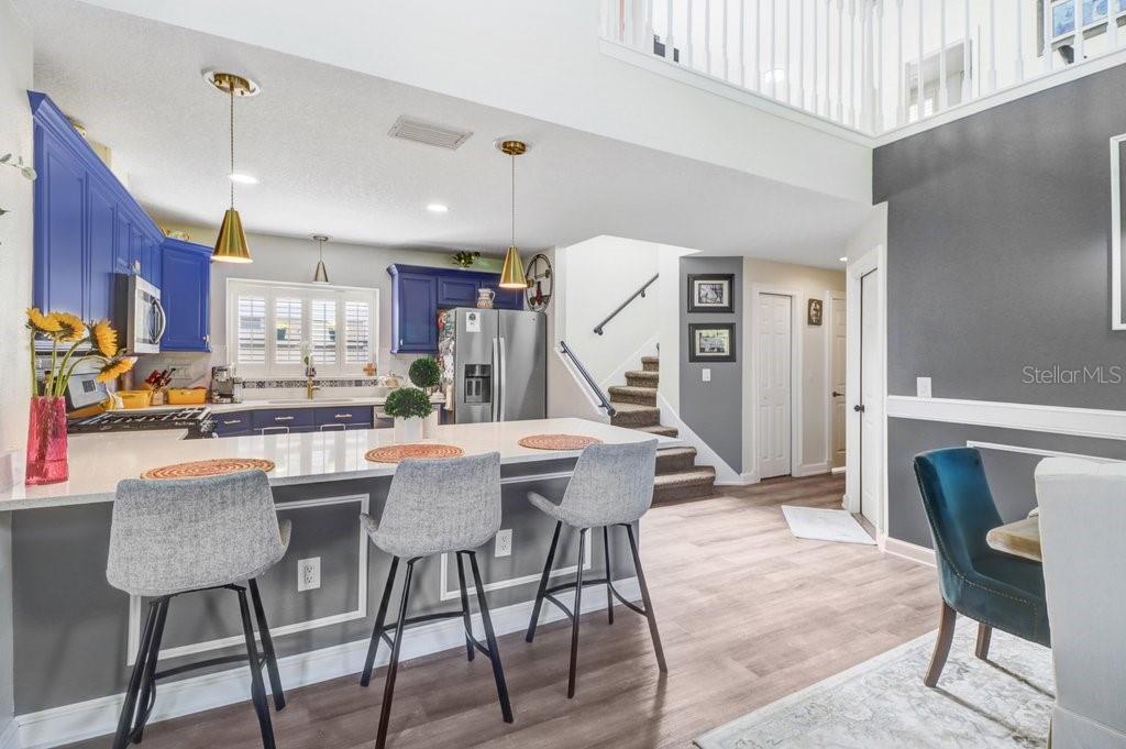 A kitchen with blue cabinets and a breakfast bar overlooks a dining area and stairs — 6049 GENTLE BEN CIRCLE, WESLEY CHAPEL, FL
