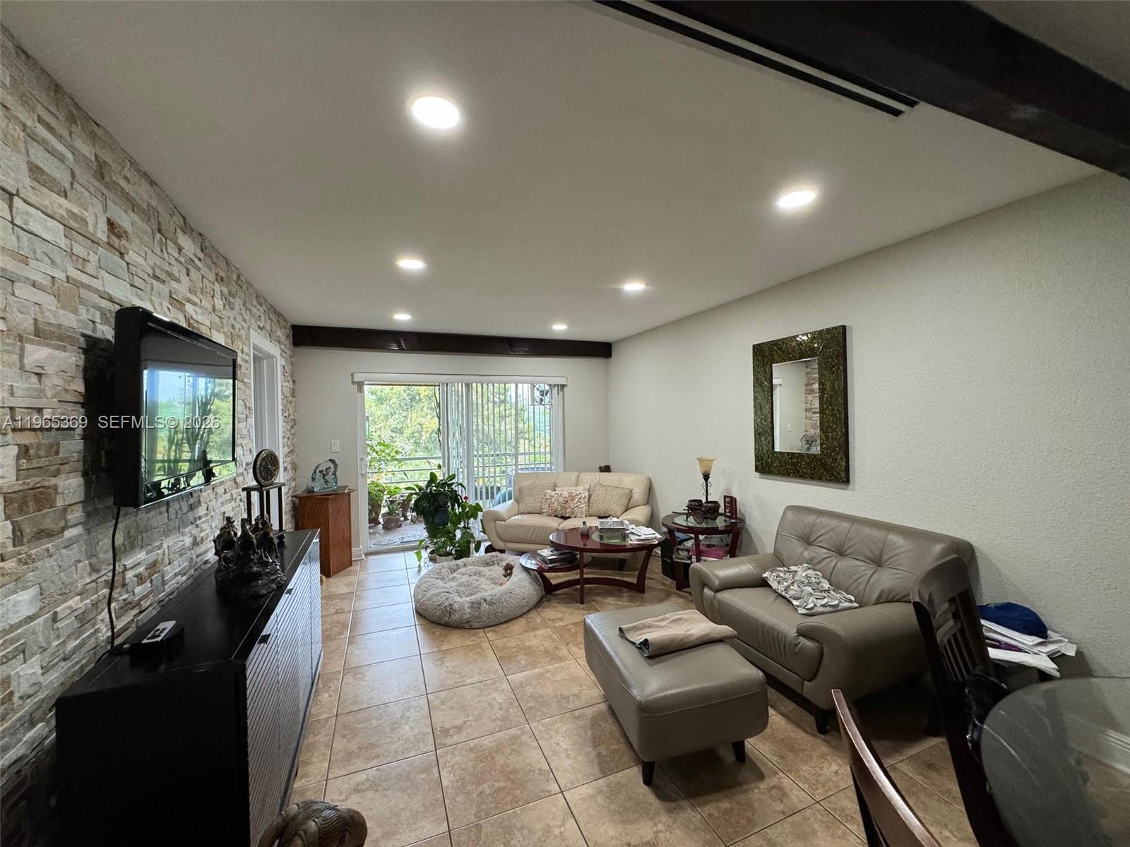 A living room features a stone accent wall, tile flooring, and a sliding glass door — 5500 SW 77th Ct # 305, Miami FL 33155, MIAMI, FL