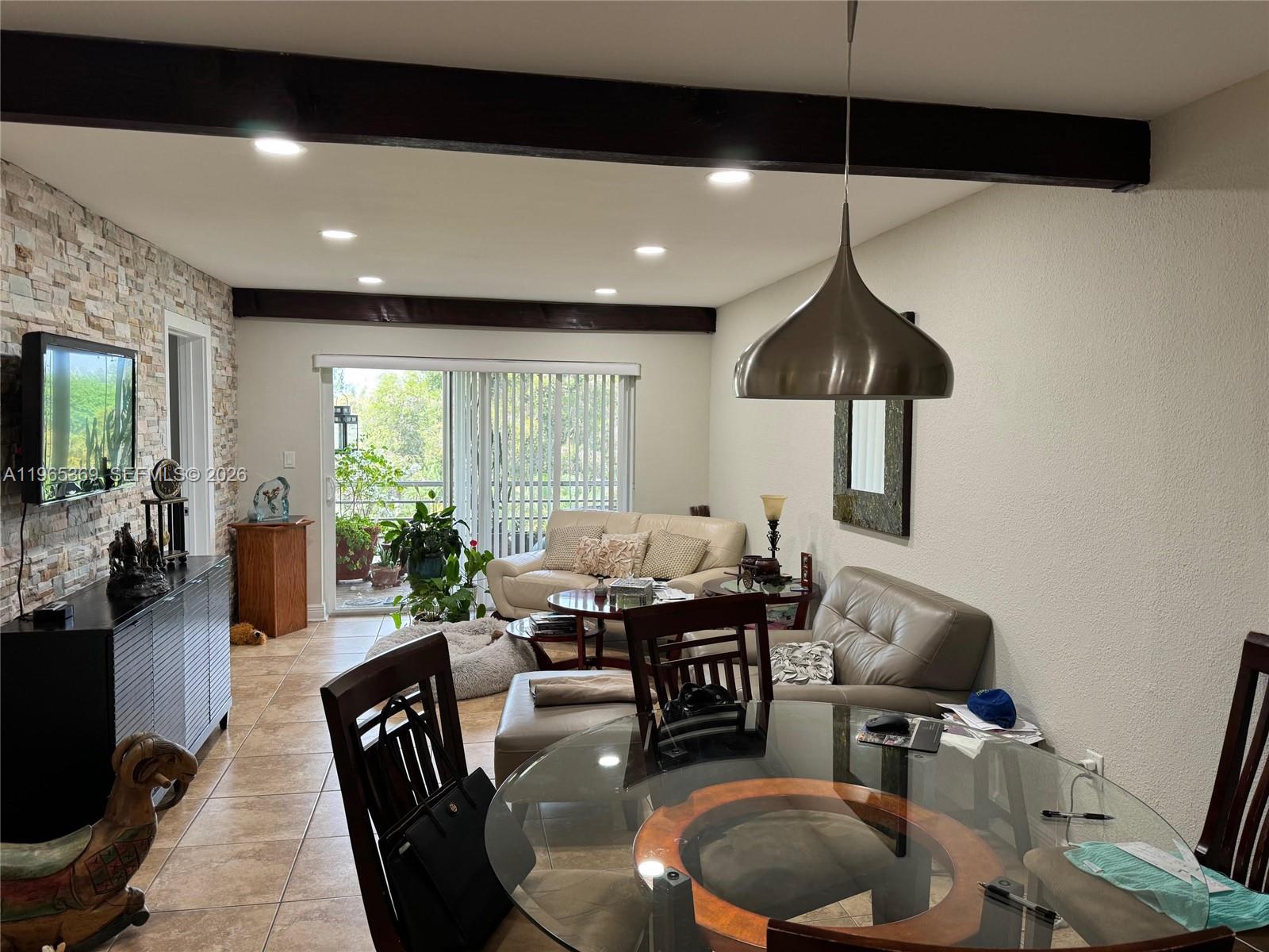 A living and dining area features a stone accent wall, exposed ceiling beams, and sliding doors — 5500 SW 77th Ct # 305, Miami FL 33155, MIAMI, FL