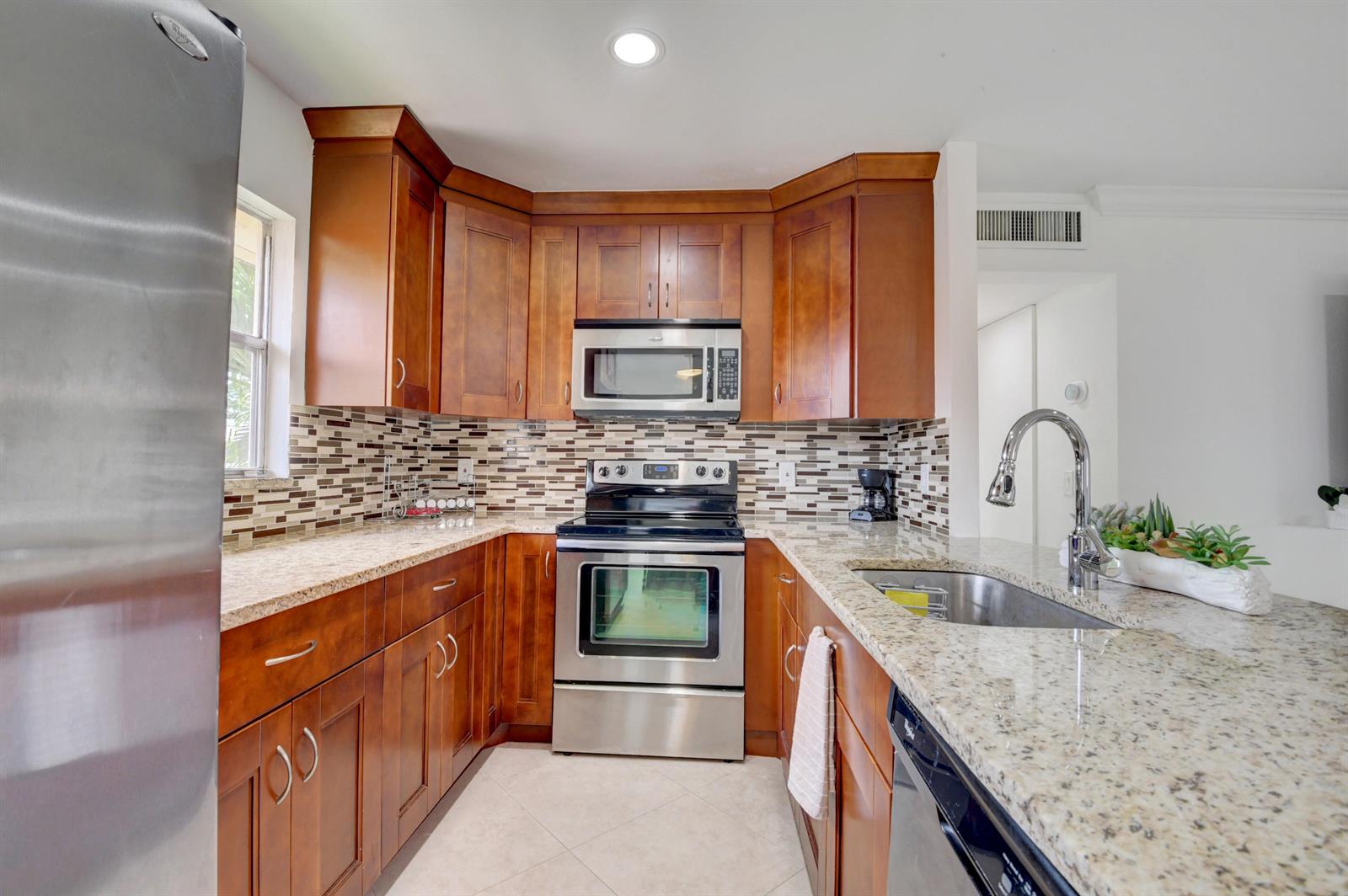 A kitchen features cherry wood cabinets, granite countertops, stainless steel appliances, and a tiled backsplash — 468 Saxony Way, Delray Beach FL 33446, DELRAY BEACH, FL