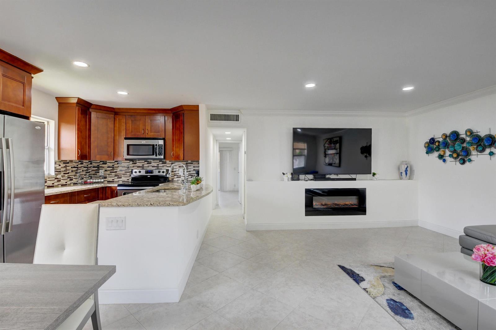 An open-concept kitchen and living area featuring wood cabinets, a fireplace, and tile flooring — 468 Saxony Way, Delray Beach FL 33446, DELRAY BEACH, FL
