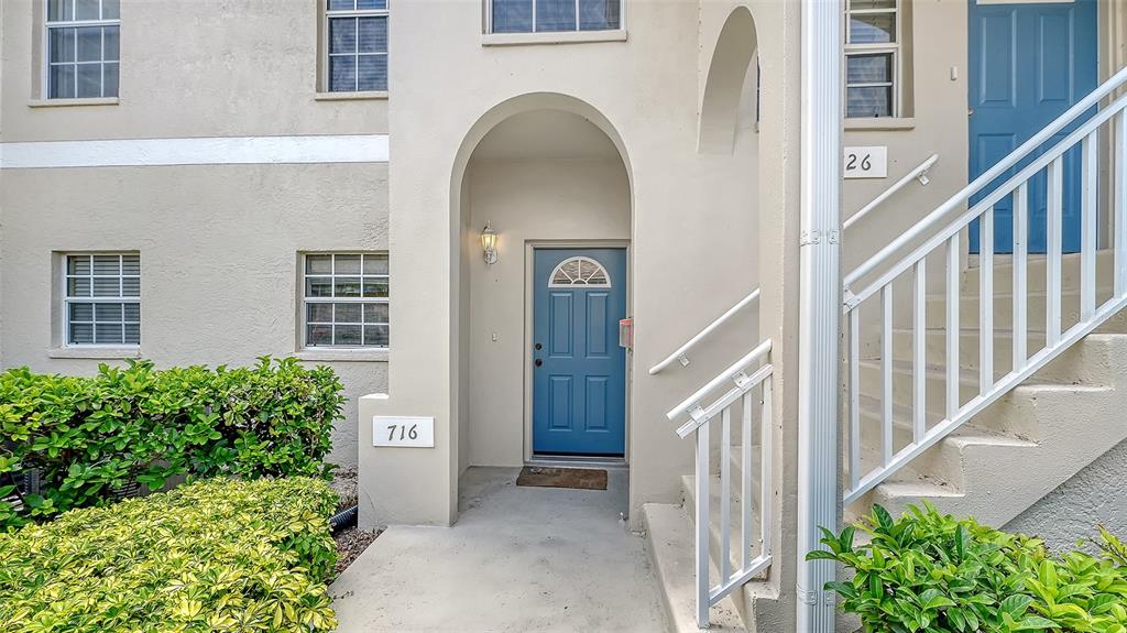 The exterior of a multi-story building features a blue front door, stairs, and landscaping — 8370 WINGATE DRIVE UNIT 716, SARASOTA, FL