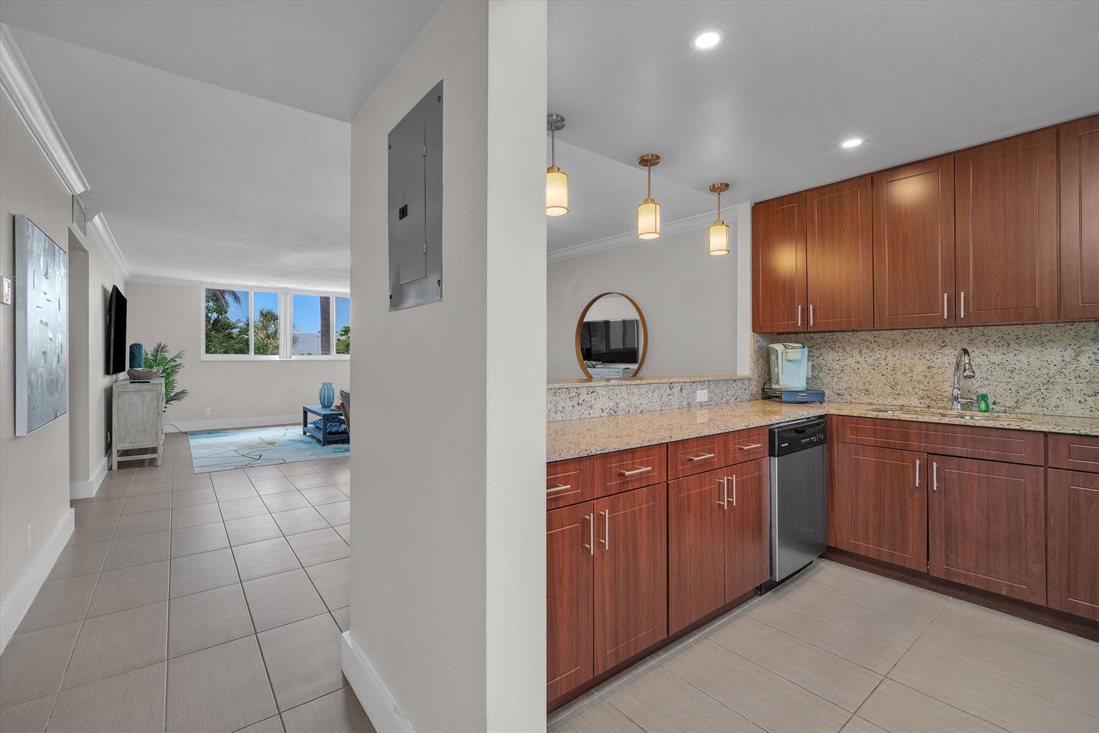 A kitchen with wood cabinets and granite countertops opens to a living area with tile — 601 N Ocean Boulevard # 203, Boca Raton FL 33432, BOCA RATON, FL