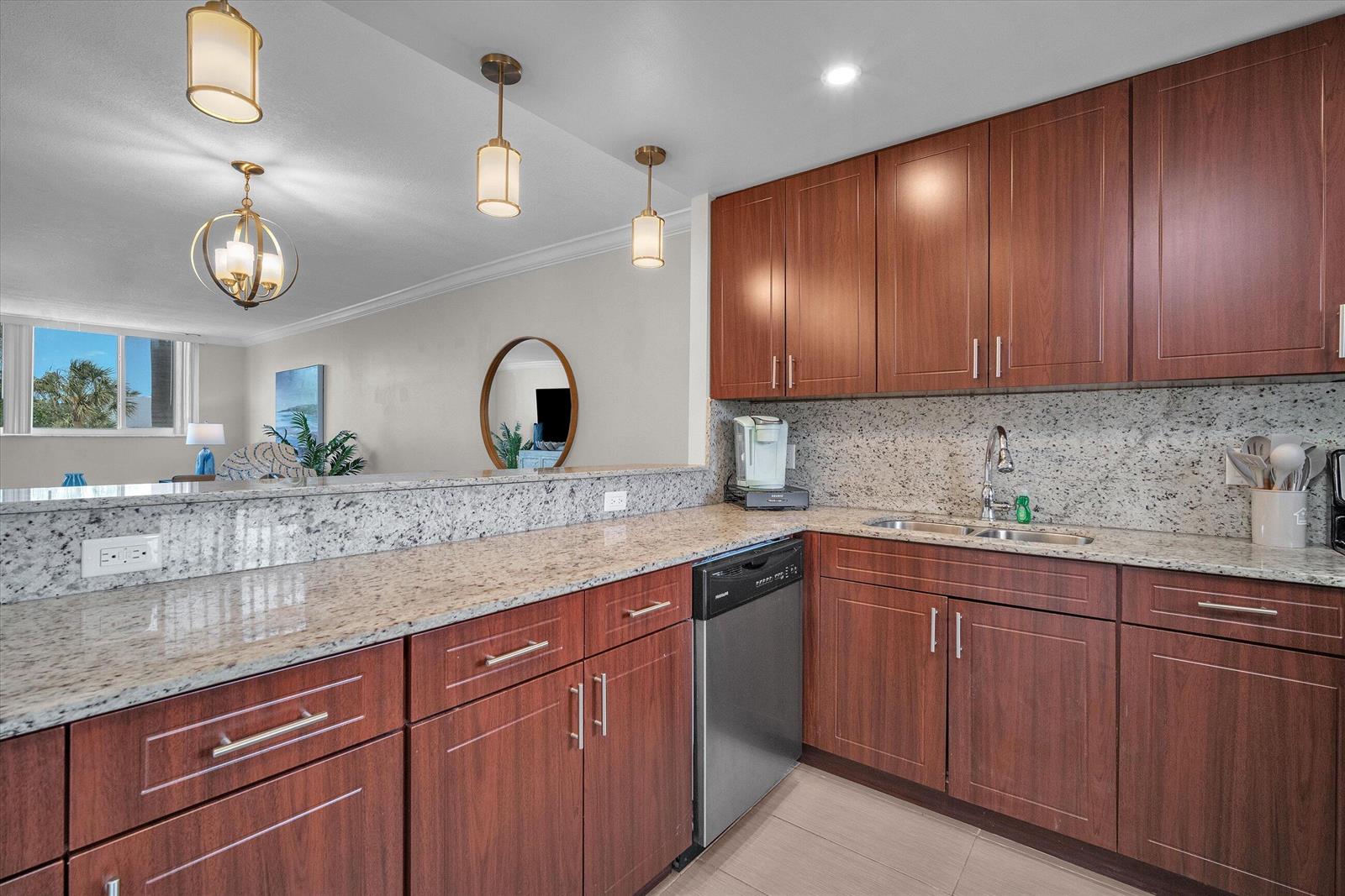 A kitchen with wood cabinets, granite countertops, and a stainless steel dishwasher overlooks a living area — 601 N Ocean Boulevard # 203, Boca Raton FL 33432, BOCA RATON, FL