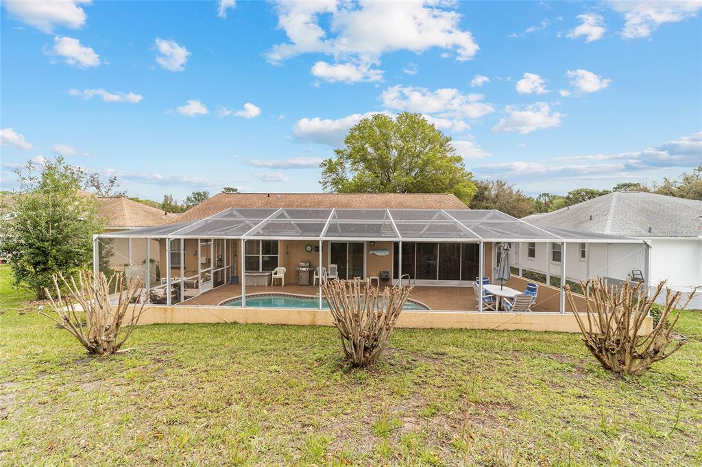 A backyard view of a house with a screened-in pool enclosure and three pruned bushes — 11534 SW 74TH COURT, OCALA, FL