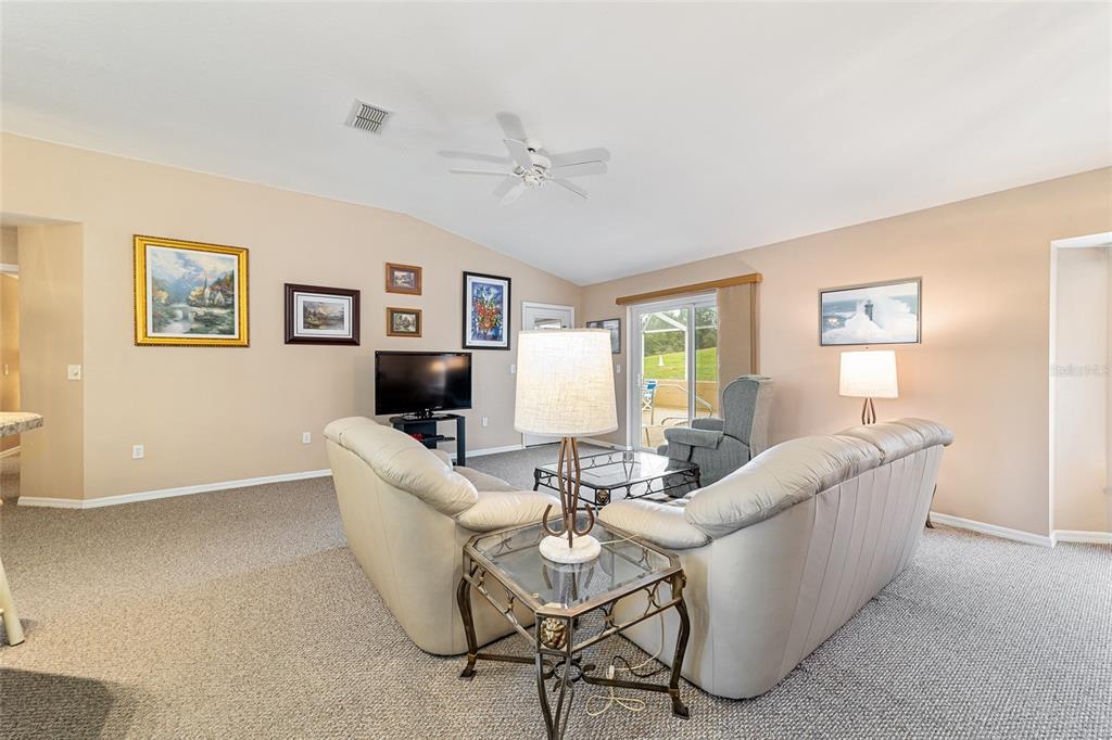 A living room features beige walls, carpeted flooring, a ceiling fan, and two light-colored sofas — 11534 SW 74TH COURT, OCALA, FL