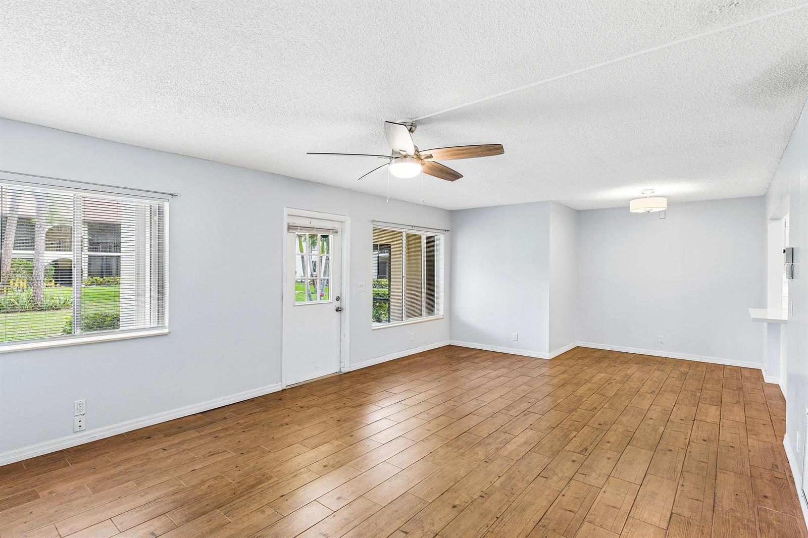 An empty living room features light blue walls, wood-look tile flooring, and a ceiling fan — 3560 Pine Tree Court # 1, FL 33463, FL