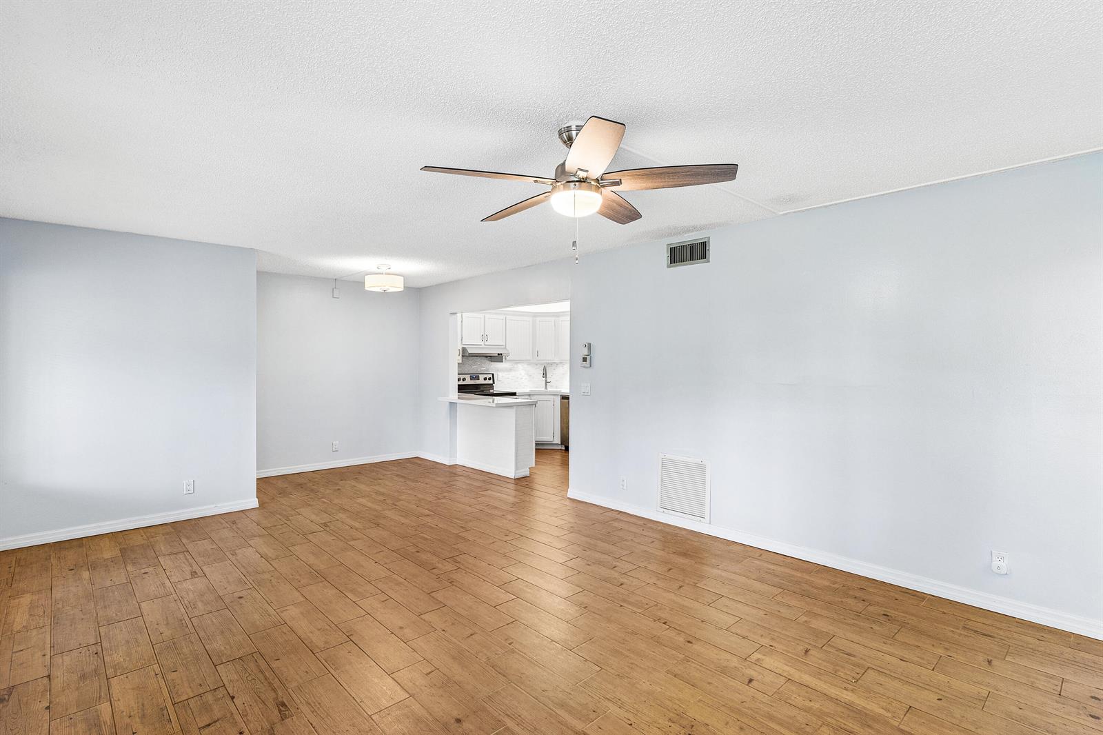 An empty living room with wood-look tile flooring, a ceiling fan, and an open kitchen — 3560 Pine Tree Court # 1, FL 33463, FL