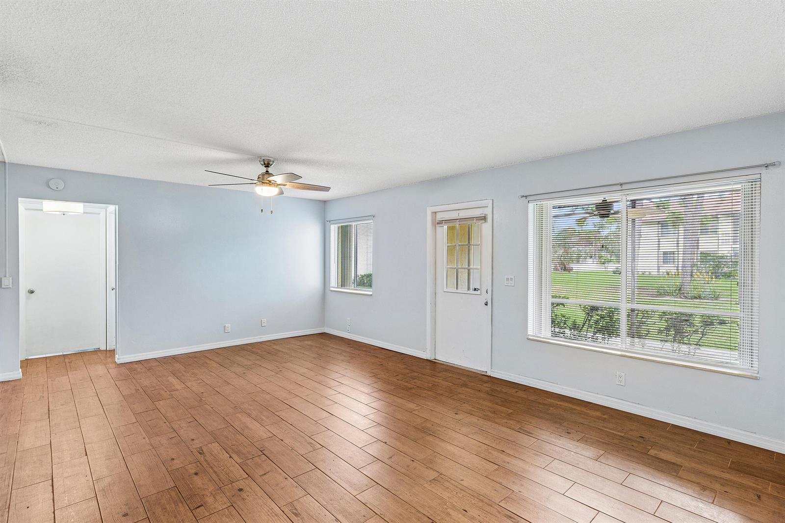 An empty living room features light blue walls, wood-look tile flooring, and a ceiling fan — 3560 Pine Tree Court # 1, FL 33463, FL