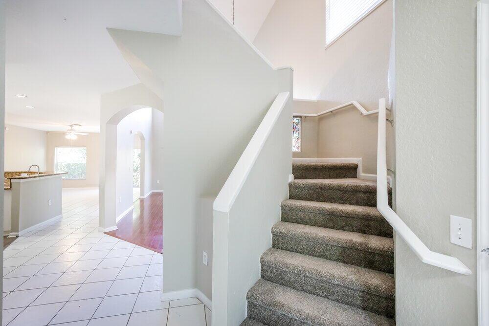 A carpeted staircase with a white handrail leads upward next to a tiled entryway — CORAL SPRINGS, FL