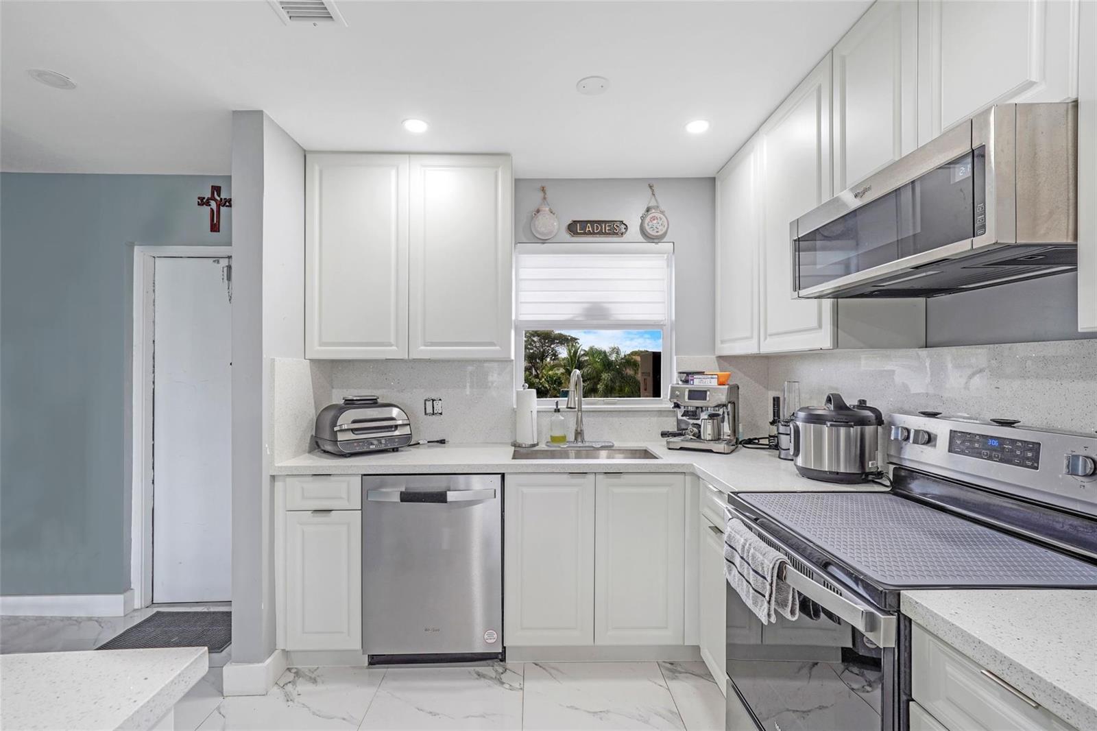 A kitchen features white cabinets, stainless steel appliances, quartz countertops, and marble-style tile flooring — 6650 Royal Palm Boulevard # 306c, Pompano Beach FL 33063, POMPANO BEACH, FL