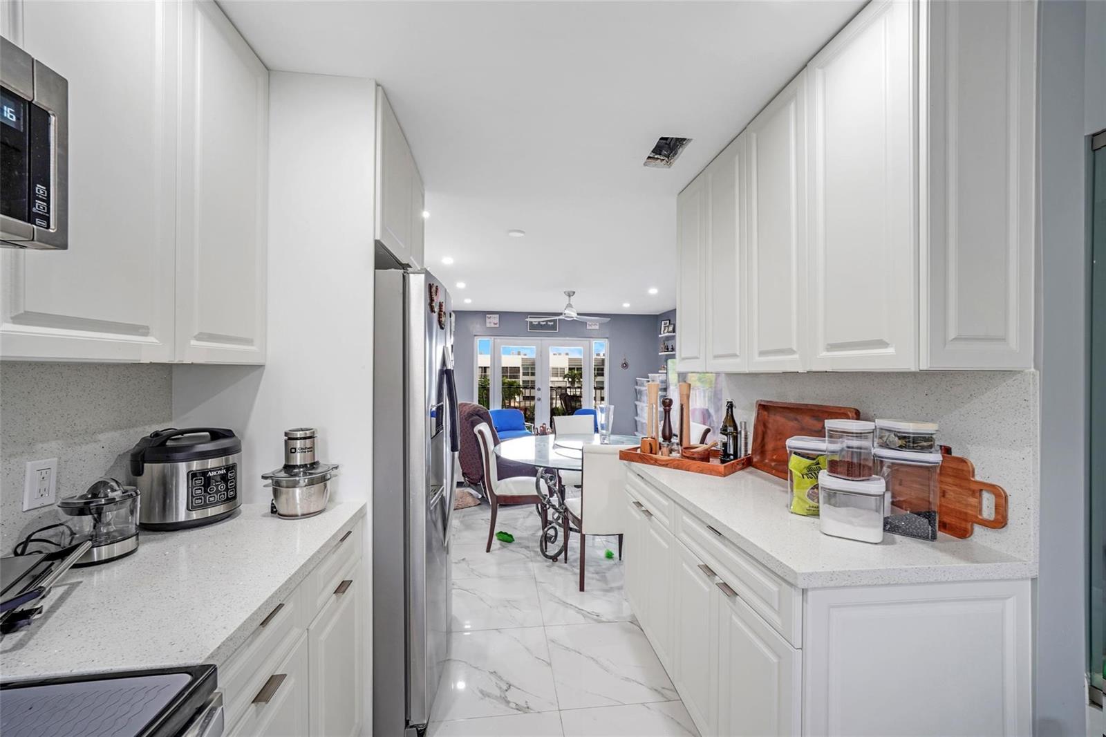 A galley kitchen with white cabinets and quartz countertops opens into a dining area — 6650 Royal Palm Boulevard # 306c, Pompano Beach FL 33063, POMPANO BEACH, FL