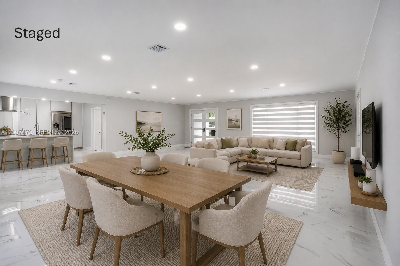 A staged open-concept living and dining area features marble floors, neutral furniture, and a kitchen — 19150 S Saint Andrews Dr, Hialeah FL 33015, HIALEAH, FL